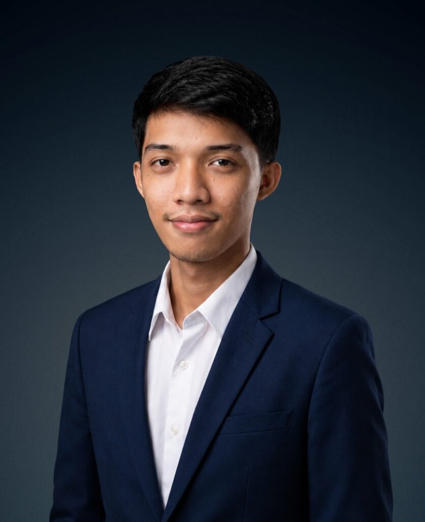 Professional headshot of a young man in a navy blazer and white shirt, against a dark gradient backdrop.